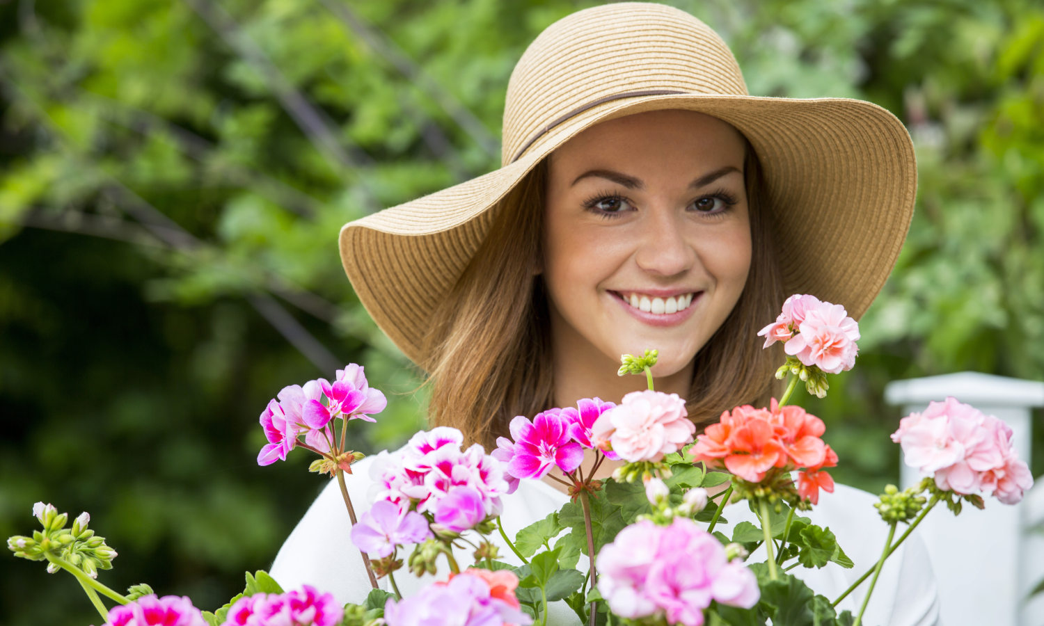 Lächelnde Frau mit pinke, orangenen und rosa Geranien und Flechthut